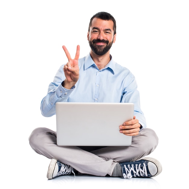 Hombre con la computadora portátil que hace gesto de la victoria