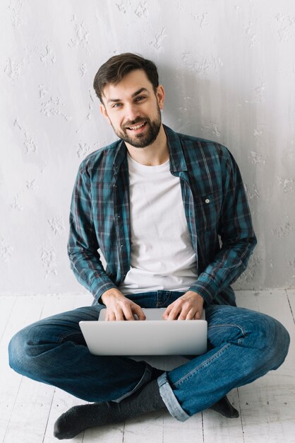 Hombre con la computadora portátil que se sienta cerca de la pared