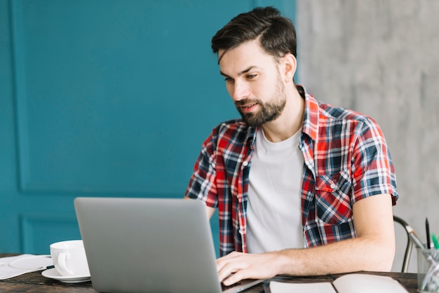 Hombre con la computadora portátil que se sienta en la tabla