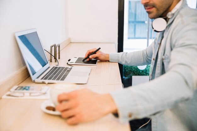 Hombre en la computadora portátil con tableta tomando café