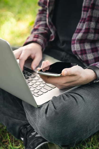 Un hombre con una computadora portátil y un teléfono inteligente se sienta en el primer plano de la hierba