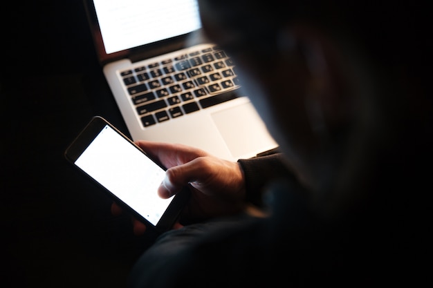 Hombre concentrado con computadora portátil y teléfono