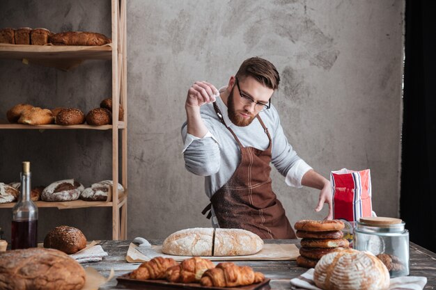 Hombre concentrado panadero de pie en la panadería cerca de pan