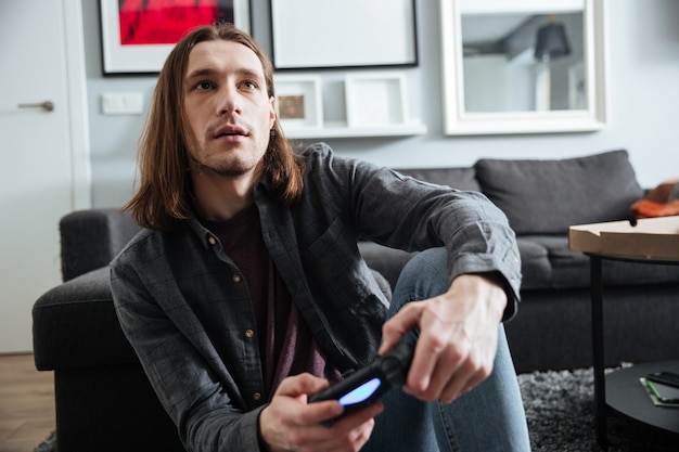 Hombre concentrado sentado en su casa en el interior jugar con joystick