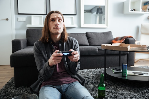 Hombre concentrado sentado en su casa en el interior jugar con joystick