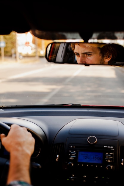 Hombre conduciendo un automóvil visto a través del espejo retrovisor