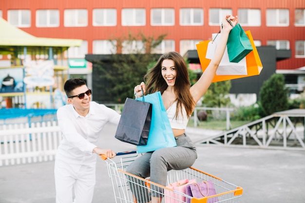 Hombre conduciendo carro de compras con mujer feliz