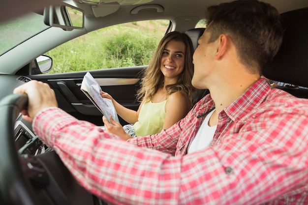 Hombre conduciendo el coche mirando a la mujer sosteniendo el mapa