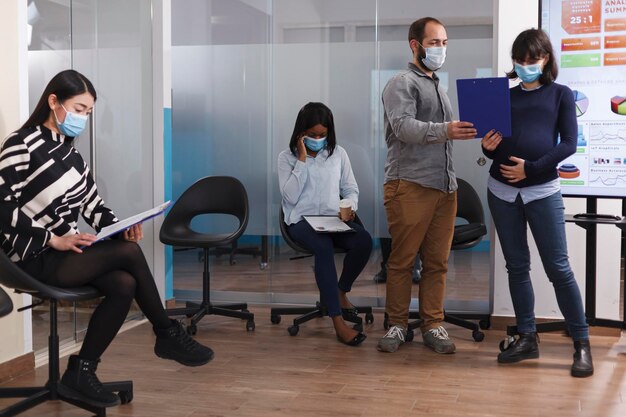 Hombre confiado entregando el currículum vítae al gerente embarazada mientras habla de la experiencia laboral en la sala de espera. Gente culturalmente diversa en el área del vestíbulo leyendo la hoja de deberes y las normas internas de la empresa