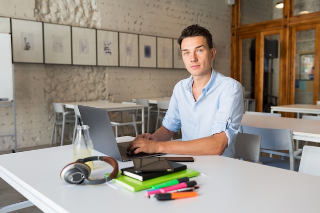 Hombre confiado joven que trabaja en la computadora portátil, sentado en la oficina de coworking