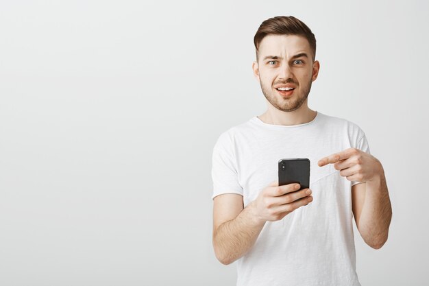 Hombre confundido apuntando al teléfono móvil y preguntando sobre la aplicación