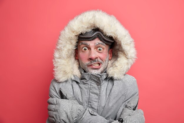 El hombre congelado tiembla de frío tiene la cara roja cubierta por una barba helada de hielo usa chaqueta con capucha necesita calentarse durante la expedición de invierno.