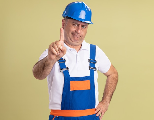 Hombre constructor adulto confiado en uniforme muestra el dedo índice en verde oliva