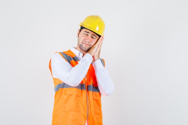 Hombre constructor apoyado en las palmas de las manos como almohada en camisa, uniforme y con sueño. vista frontal.