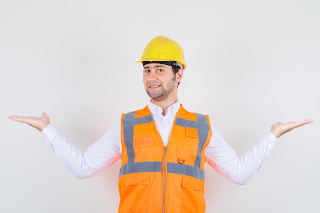 Hombre constructor en camisa, uniforme extendiendo los brazos como si estuviera atrapando algo y luciendo feliz, vista frontal.