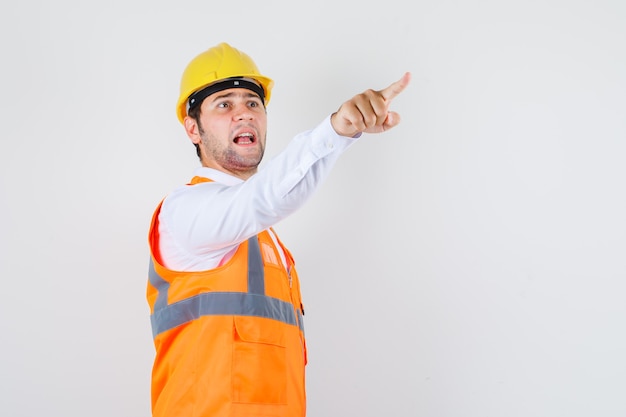 Hombre constructor en camisa, uniforme mostrando algo y mirando preocupado, vista frontal.