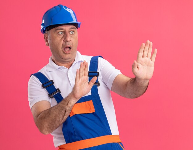 Hombre constructor caucásico adulto ansioso en uniforme estirando las manos aisladas