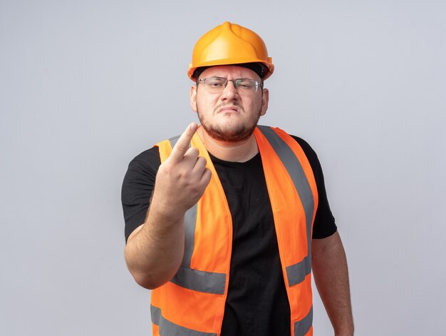 Hombre constructor en chaleco de construcción y casco de seguridad mirando a la cámara con cara enojada gesticulando con la mano como discutiendo sobre blanco