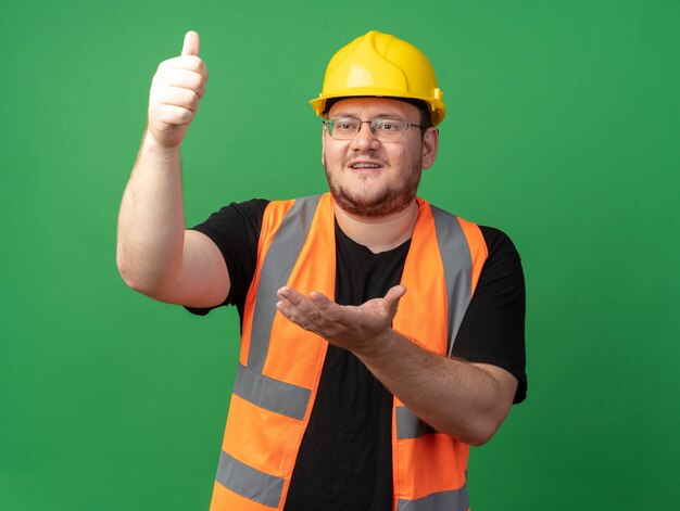 Hombre constructor en chaleco de construcción y casco de seguridad mirando a un lado feliz y confiado con el brazo hacia arriba mostrando los pulgares para arriba