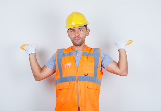 Foto gratuita hombre constructor levantando los brazos y mirando a cámara en uniforme, casco, guantes, vista frontal.