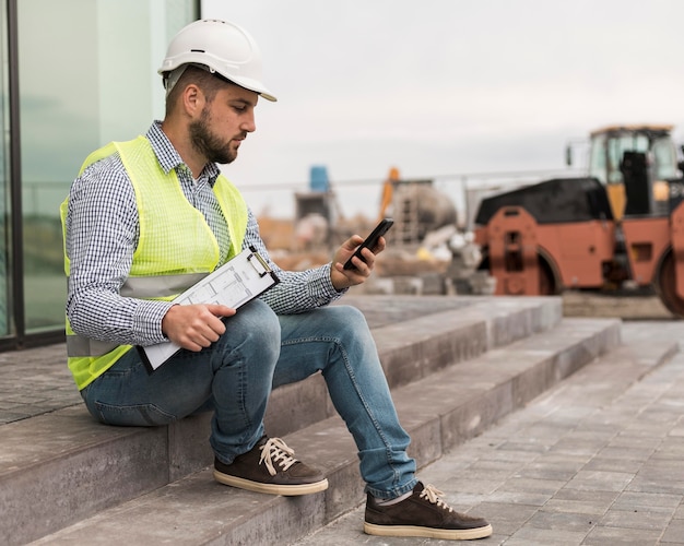 Foto gratuita hombre constructor de tiro completo sentado en las escaleras