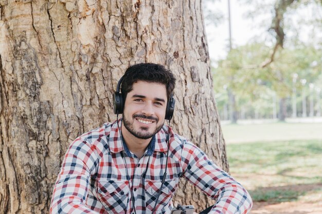 Hombre contento en auriculares posando bajo el árbol