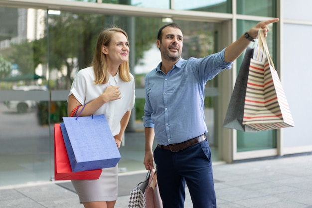 Hombre contento de compras con esposa y mostrándole algo al aire libre