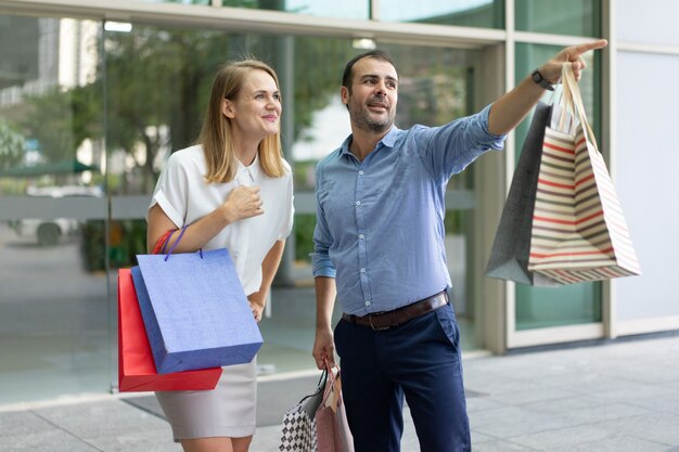 Hombre contento de compras con esposa y mostrándole algo al aire libre