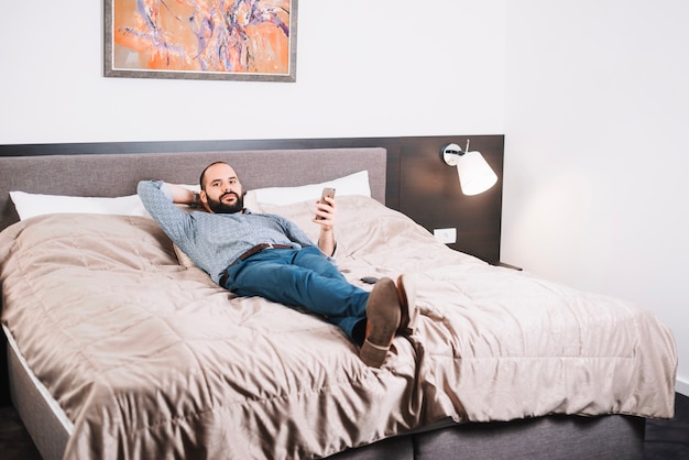 Hombre contento con teléfono posando en la cama