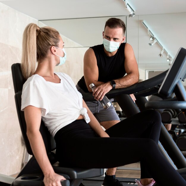 Hombre conversando con mujer en el gimnasio mientras usa máscara médica