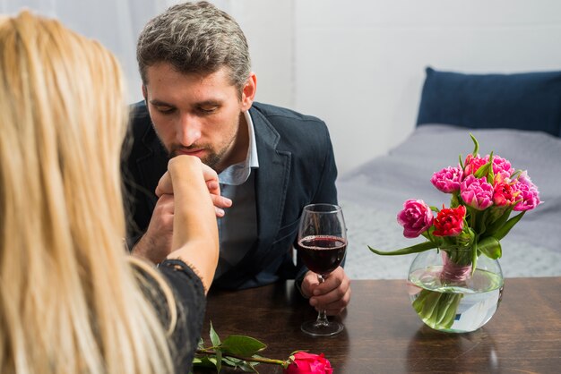 Hombre con copa de vino besando mano de mujer en mesa