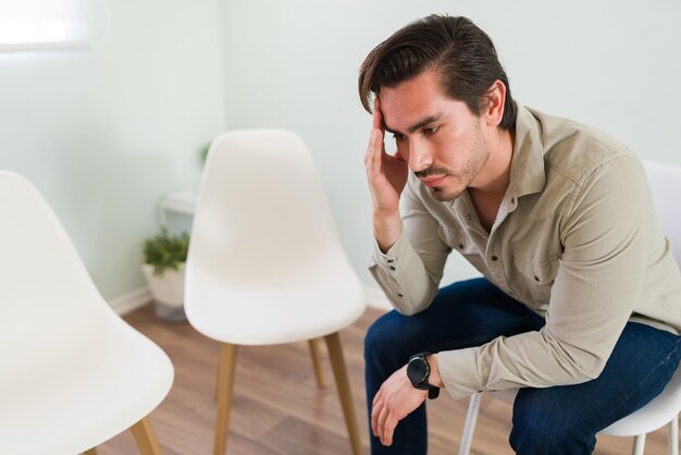 Hombre con el corazón roto de unos 20 años sintiéndose solo. Atractivo joven miembro de un grupo de apoyo pensando en hablar con un consejero de salud mental