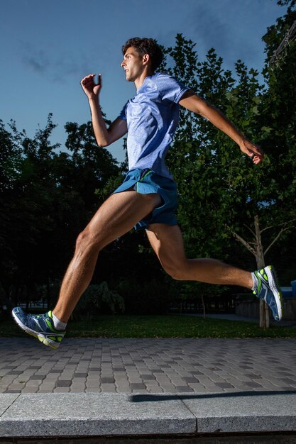 Hombre corriendo en el parque de la ciudad al atardecer. Ropa deportiva azul, shorts y camiseta.