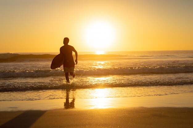 Hombre corriendo con tabla de surf en la playa