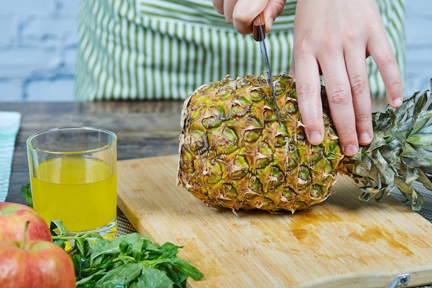 El hombre corta una manzana fresca sobre una tabla de cortar de madera junto a las manzanas y un vaso de jugo.