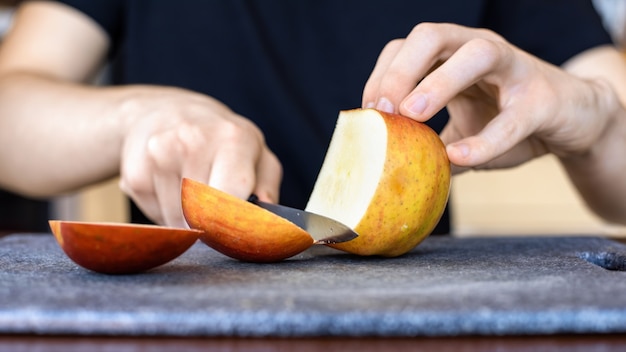 Un hombre cortando la manzana en una tabla de cocina con un cuchillo