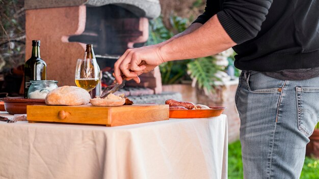 Hombre cortando pan y pollo a la parrilla con tenedor y cuchillo al aire libre