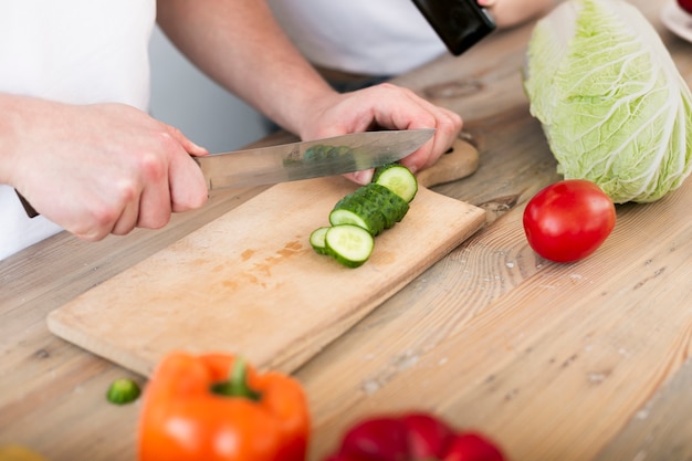 Hombre cortando el pepino en un plato de madera