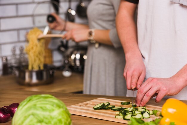 Hombre cortando pepinos y mujer cocinando pasta