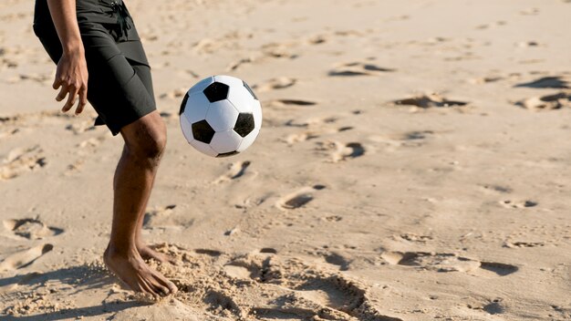 Hombre de la cosecha pateando la pelota en la playa de arena