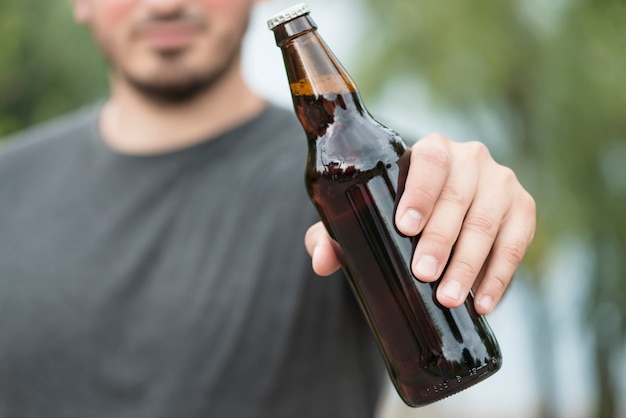 Hombre de cosecha que muestra la botella de cerveza en el parque