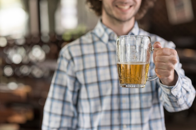 Hombre de cosecha que muestra la taza de cerveza en la barra