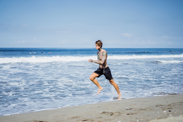 Foto gratuita un hombre en la costa del océano corriendo a lo largo de la orilla del mar