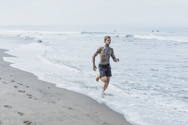 Foto gratuita un hombre en la costa del océano corriendo a lo largo de la orilla del mar