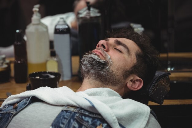 Hombre con crema de afeitar en la barba relajándose en una silla