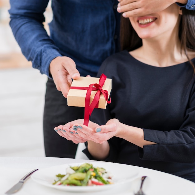 Hombre cubriendo los ojos de su novia antes de darle un primer plano de regalo