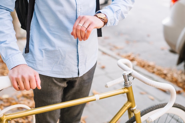 Hombre de cultivo que mira el reloj cerca de la bicicleta