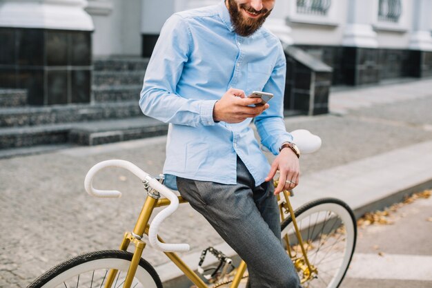 Hombre de cultivos con smartphone apoyado en bicicleta