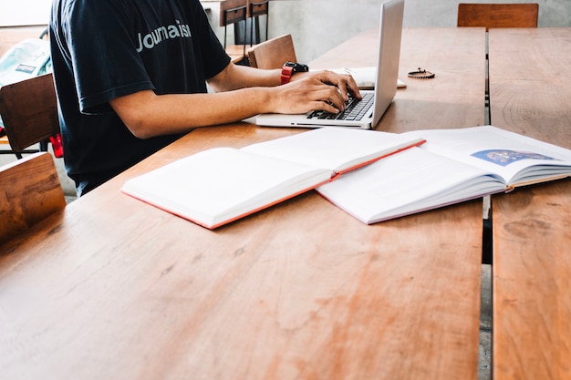 Hombre de cultivos usando una computadora portátil cerca de libros