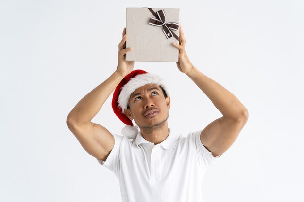 Hombre curioso con sombrero de Santa y levantando la caja de regalo sobre la cabeza